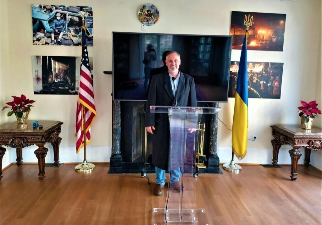 a speaker in a long, black suit, standing at a glass podium stand