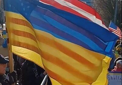 A crowd of people holding flags in front of a fence.